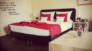 A neatly made bed with red and white bedding, a bedside table with a lamp, and a wall with framed pictures and a quote. - Henblas-Hotel (Neuenrade)