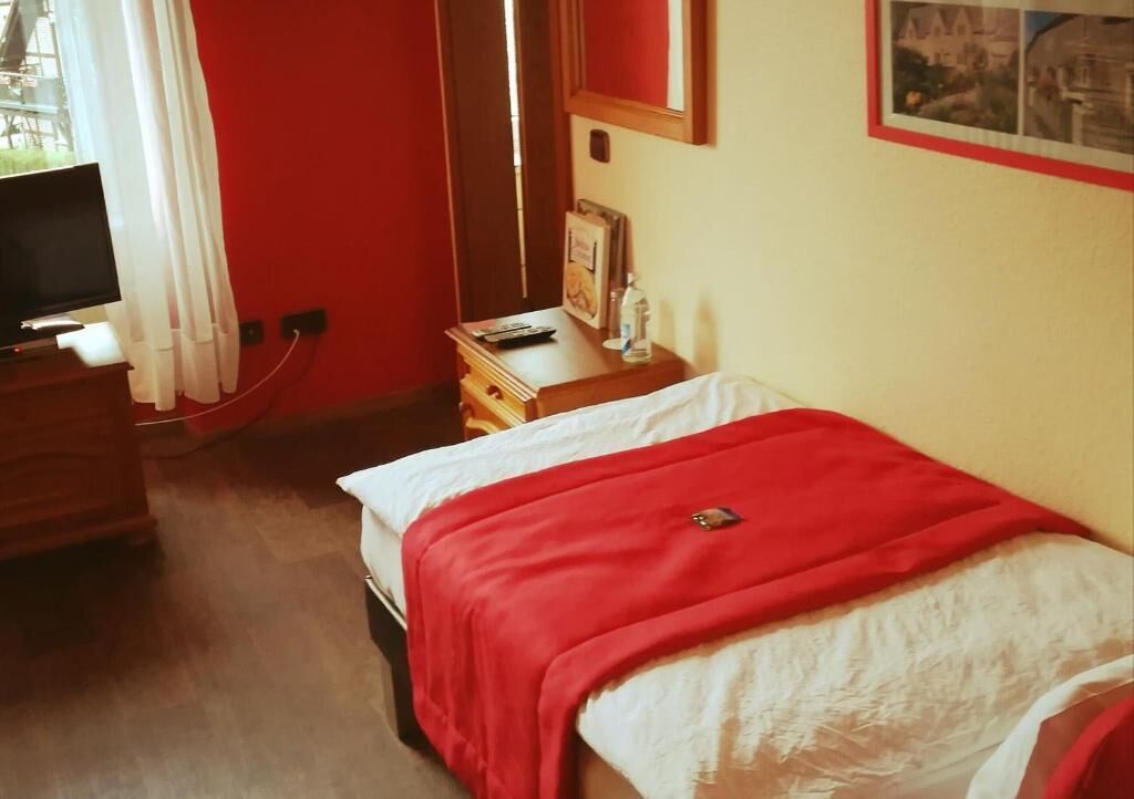 A hotel room with a bed, a wooden dresser, a television, and a red wall.
