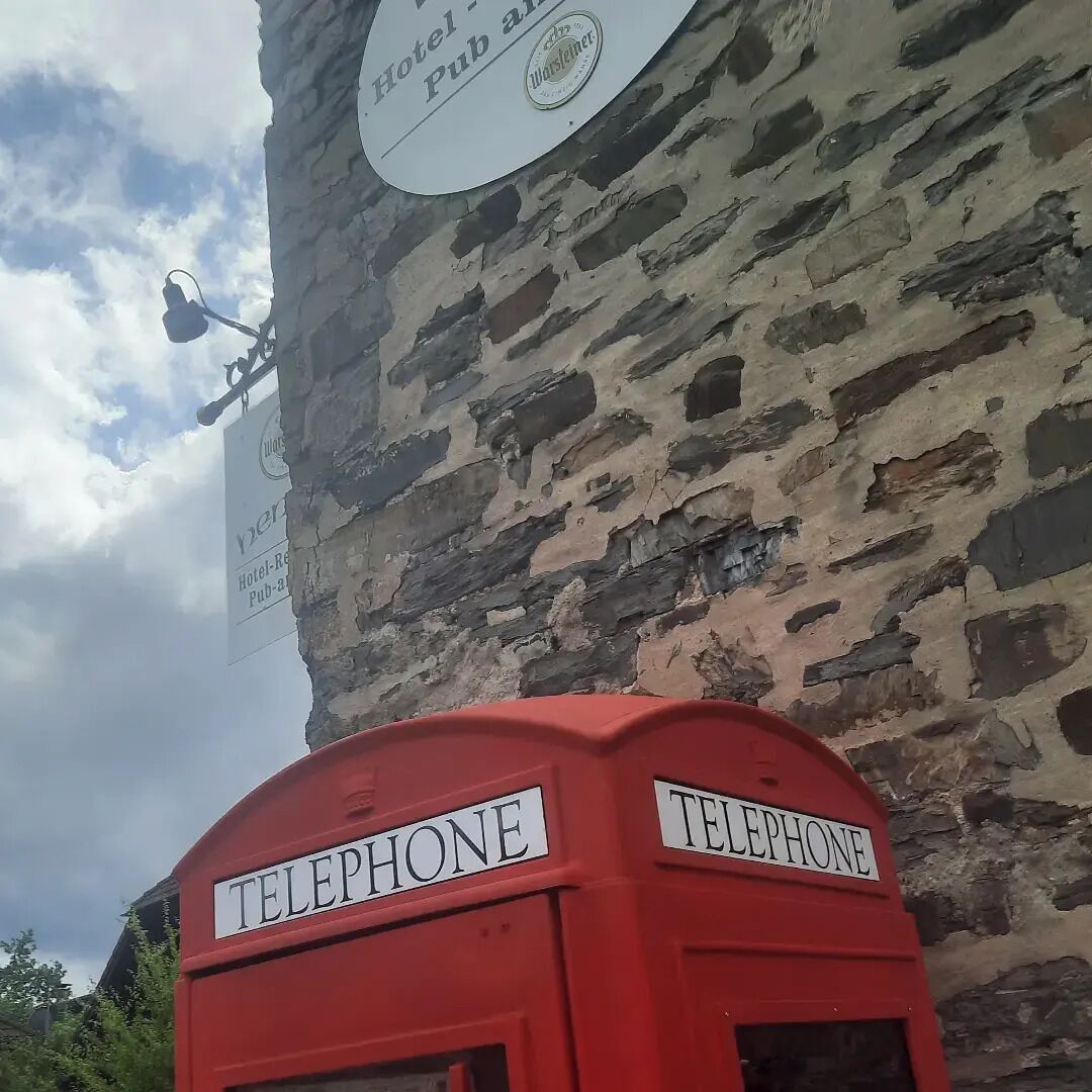 En rød telefonboks med skilte der viser ordene "TELEPHONE", foran en bygning i sten med et skilt der siger "Hotel Pub".