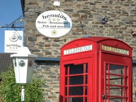 A red telephone booth and a sign for 'Henblas Hotel - Restaurant - Pub and more' against a stone wall.