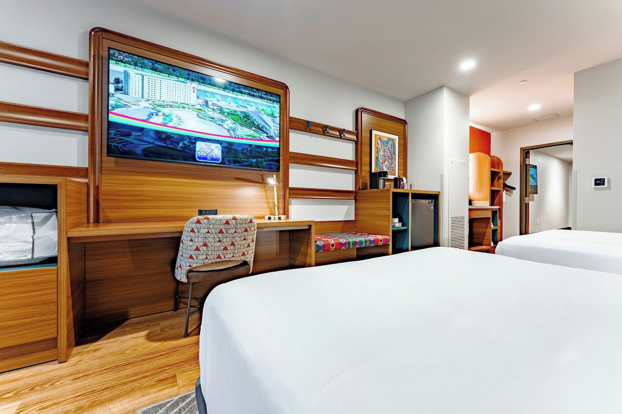 Una habitación de hotel con una televisión grande montada en la pared, un escritorio con una silla, una cama y un armario.