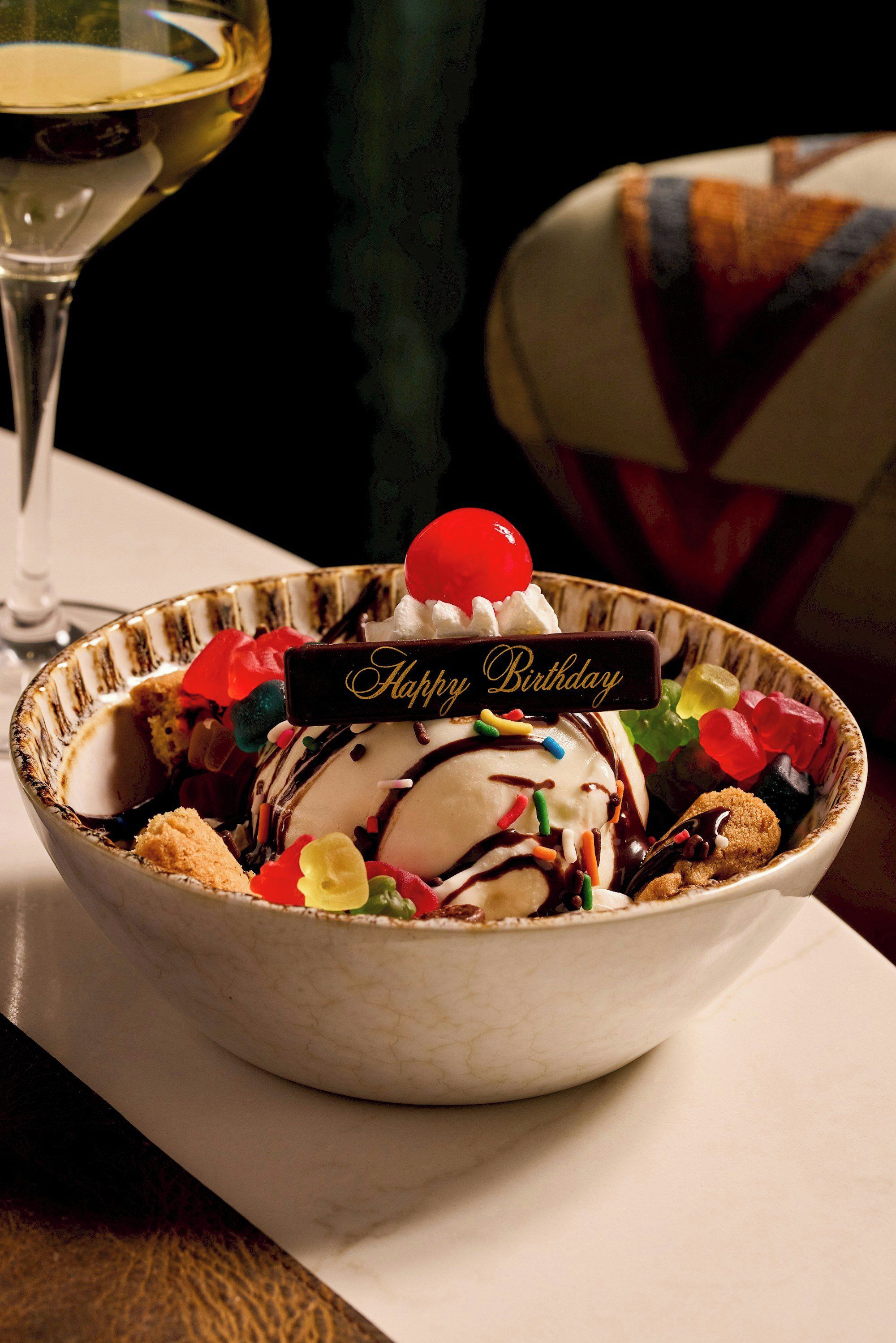 A dessert bowl with a 'Happy Birthday' sign, colorful sprinkles, and a cherry on top.