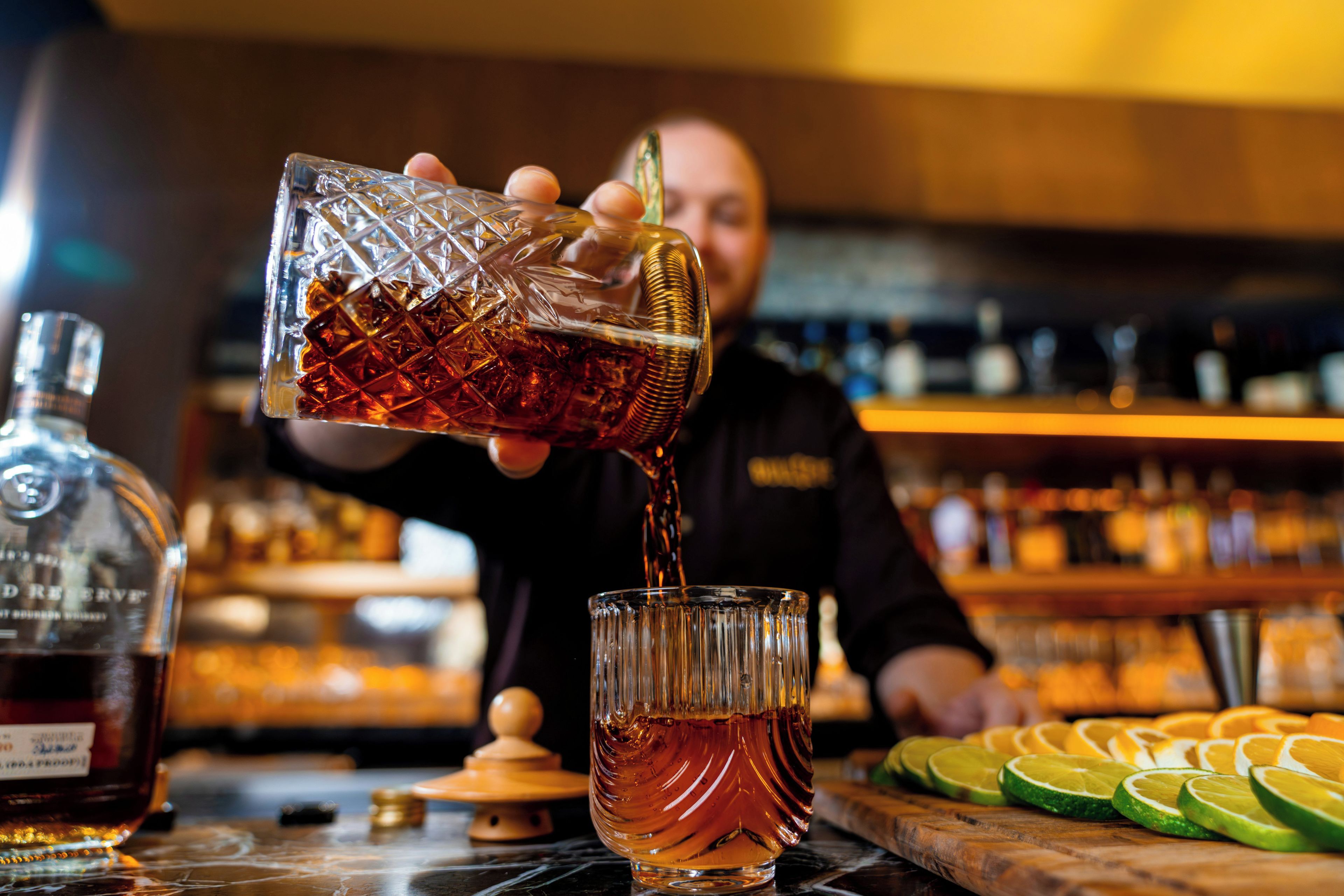Un barman verse un liquide sombre dans un verre à motifs.