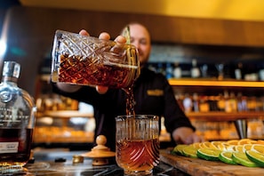 Ein Barkeeper gießt eine dunkle Flüssigkeit in ein Glas mit strukturierter Oberfläche.