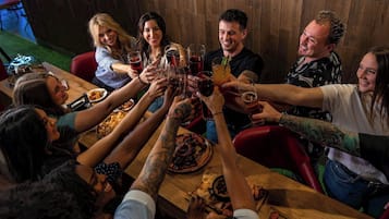 A group of people toasting with drinks around a wooden table in a room with a wooden wall.