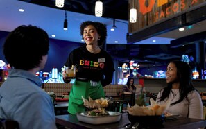 A restaurant interior with tables, chairs, and a counter where a server is serving a drink. - OKANA Resort & Indoor Waterpark (Oklahoma City)