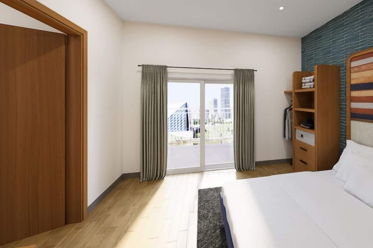 Ein Hotelzimmer mit einem großen Bett, einem Kleiderschrank, einer eingebauten Ablage und Blick auf die Stadt durch eine Schiebetür.
