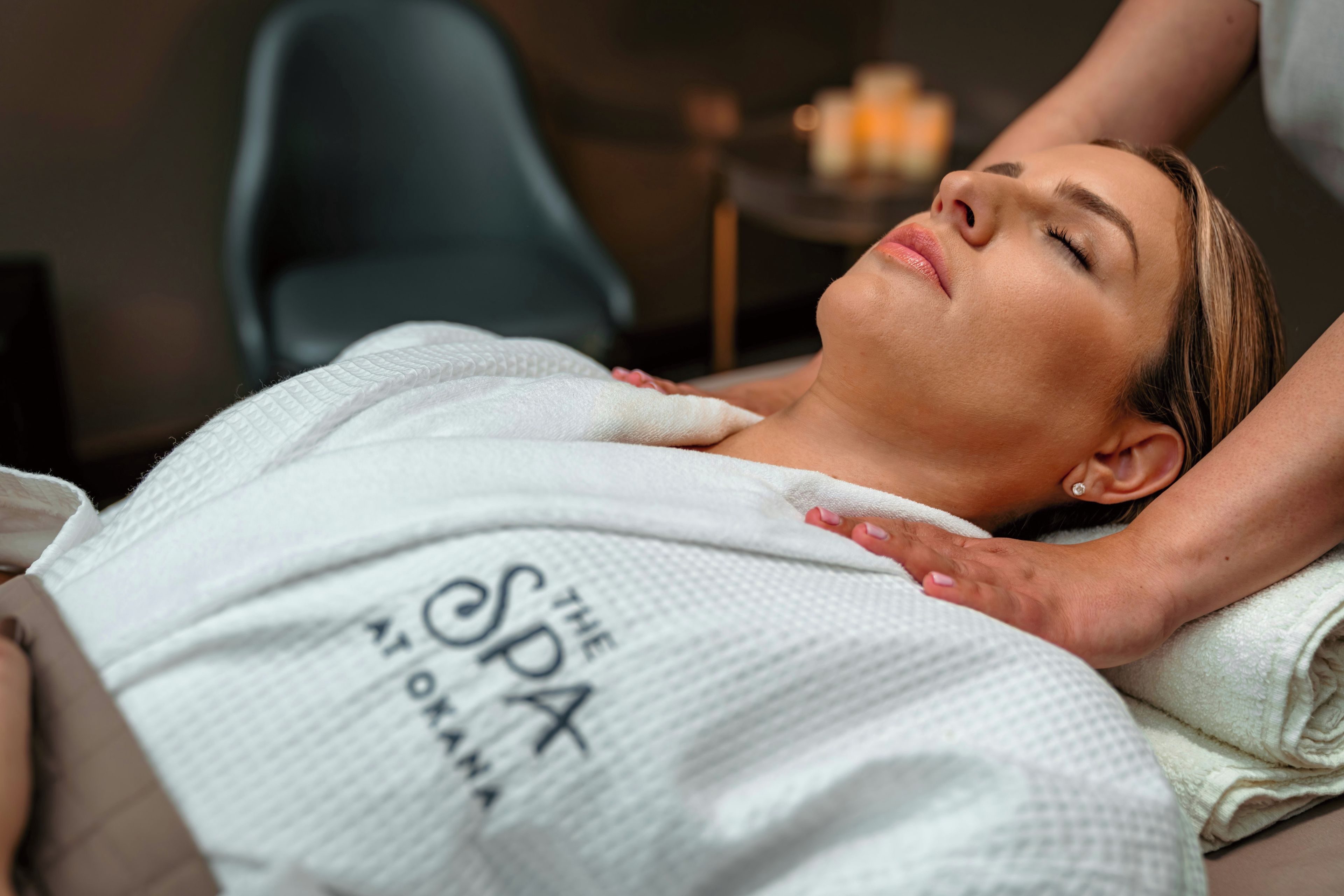 Une personne allongée sur une table de massage, le haut du corps couvert d’une serviette, et une main appliquant un soin sur son épaule.