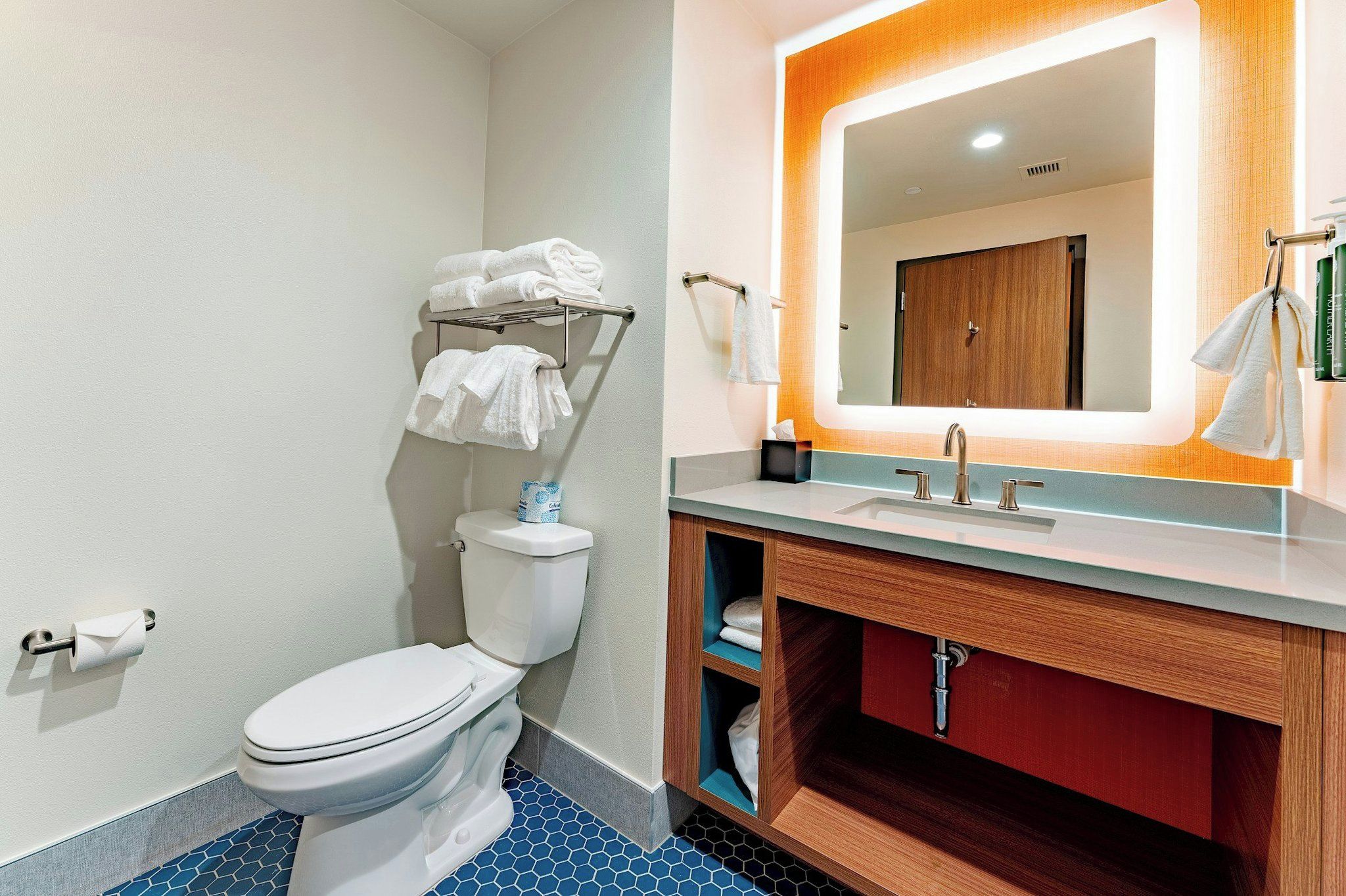 Un baño con inodoro, lavamanos, espejo y toallero.