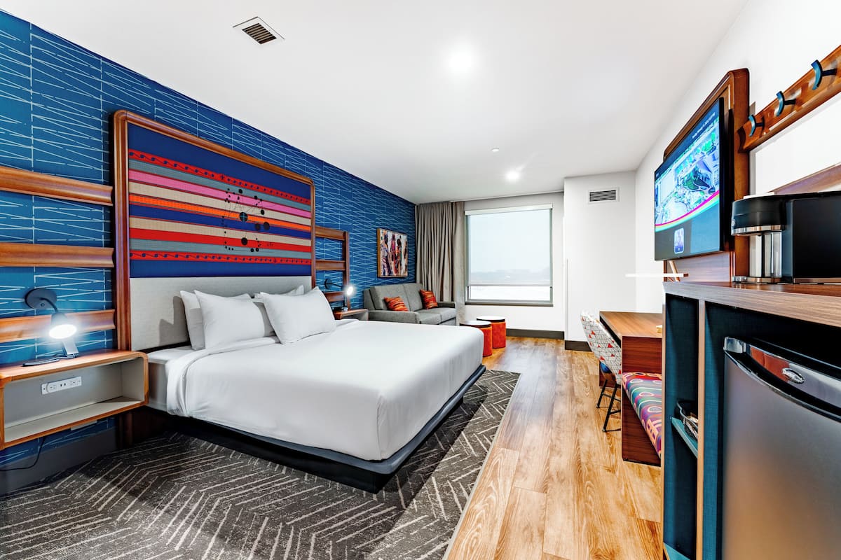 Ein modernes Hotelzimmer mit einem großen Bett, einem Schreibtisch, einem Fernseher und Blick auf die Stadt.