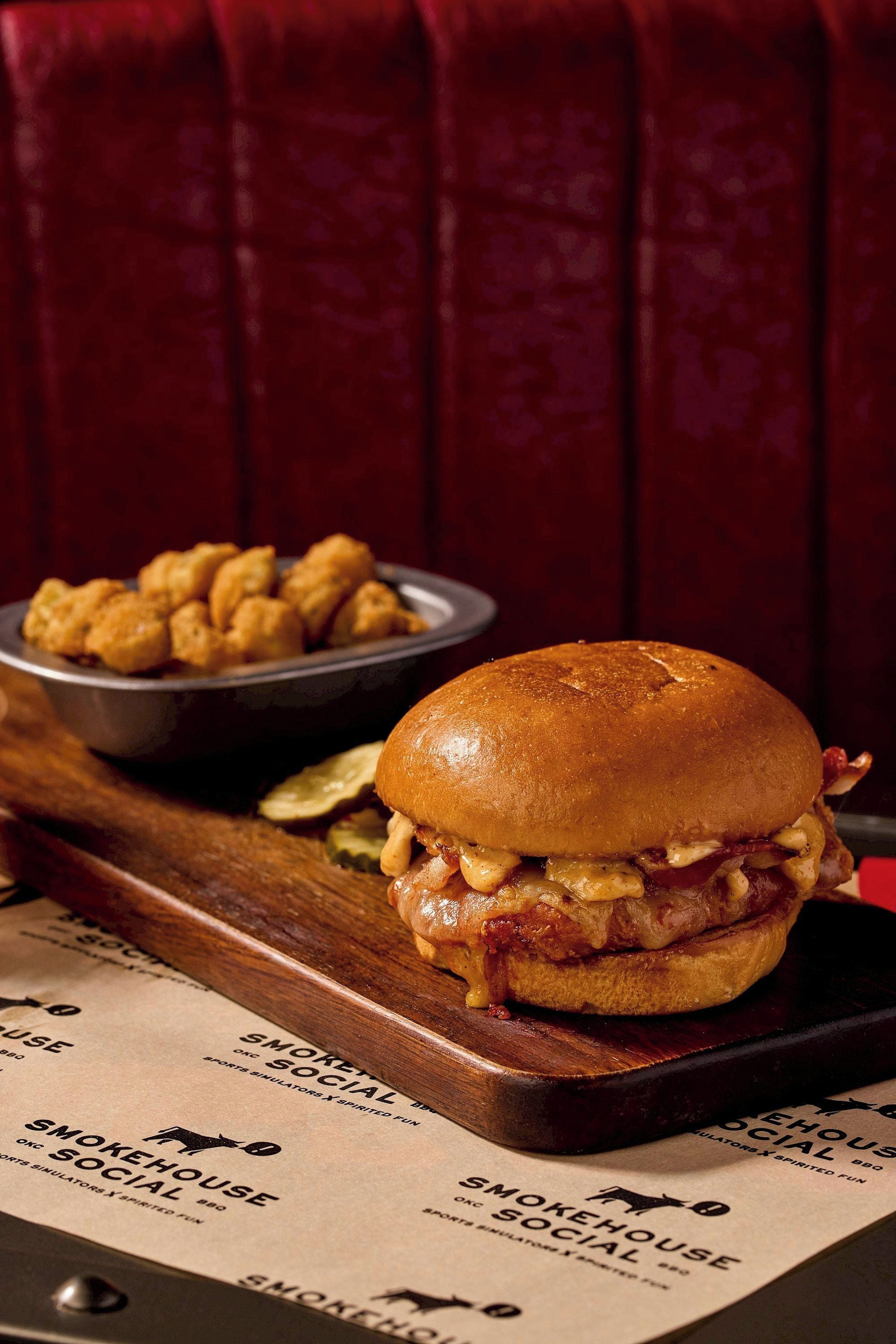 Un sándwich con pan, queso y tocino, acompañado de papas fritas, sobre una tabla de madera con un menú debajo.