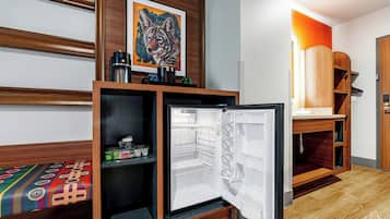 A hotel room with a bed, a small refrigerator, a wooden cabinet, and a painting on the wall.