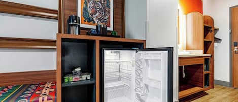 A hotel room with a bed, a small refrigerator, a wooden cabinet, and a painting on the wall.