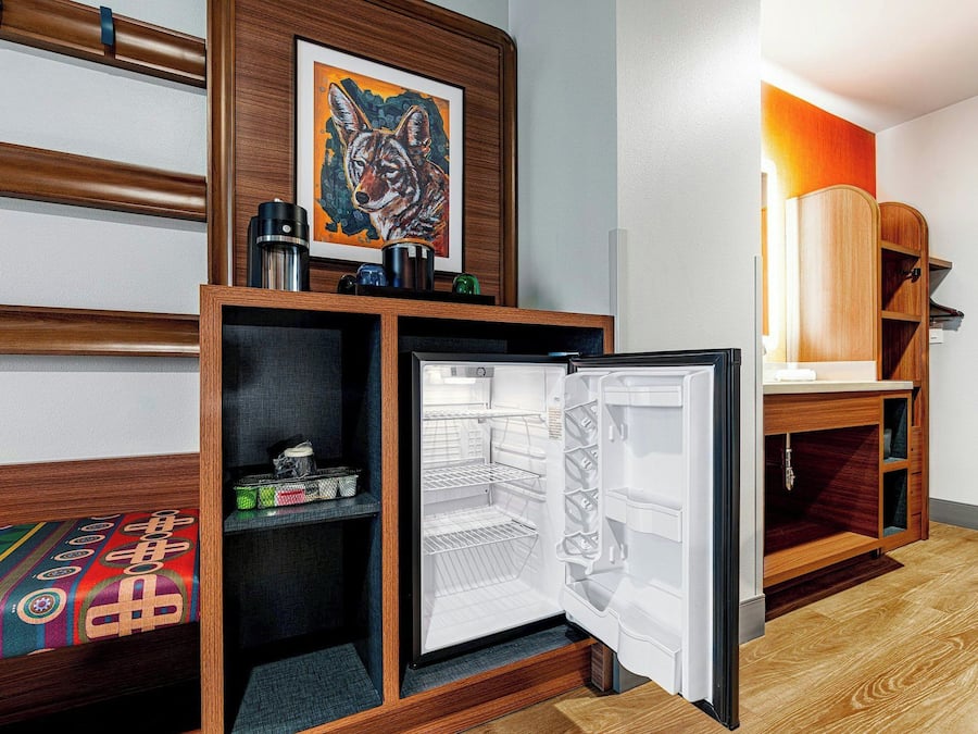Quarto de hotel com cama, pequeno frigorífico, armário de madeira e um quadro na parede.