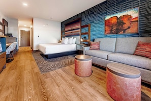 A modern hotel room with a bed, a sofa, two round side tables, and a desk with a chair. - OKANA Resort & Indoor Waterpark (Oklahoma City)