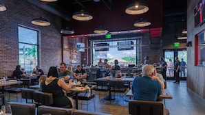 A restaurant with brick walls, large windows, and multiple dining tables and chairs. - OKANA Resort & Indoor Waterpark (Oklahoma City)