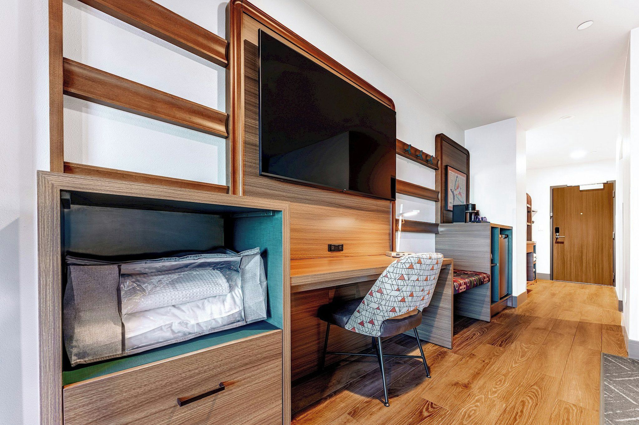 A room with built-in wooden shelves, a desk with a chair, and a large flat-screen TV.