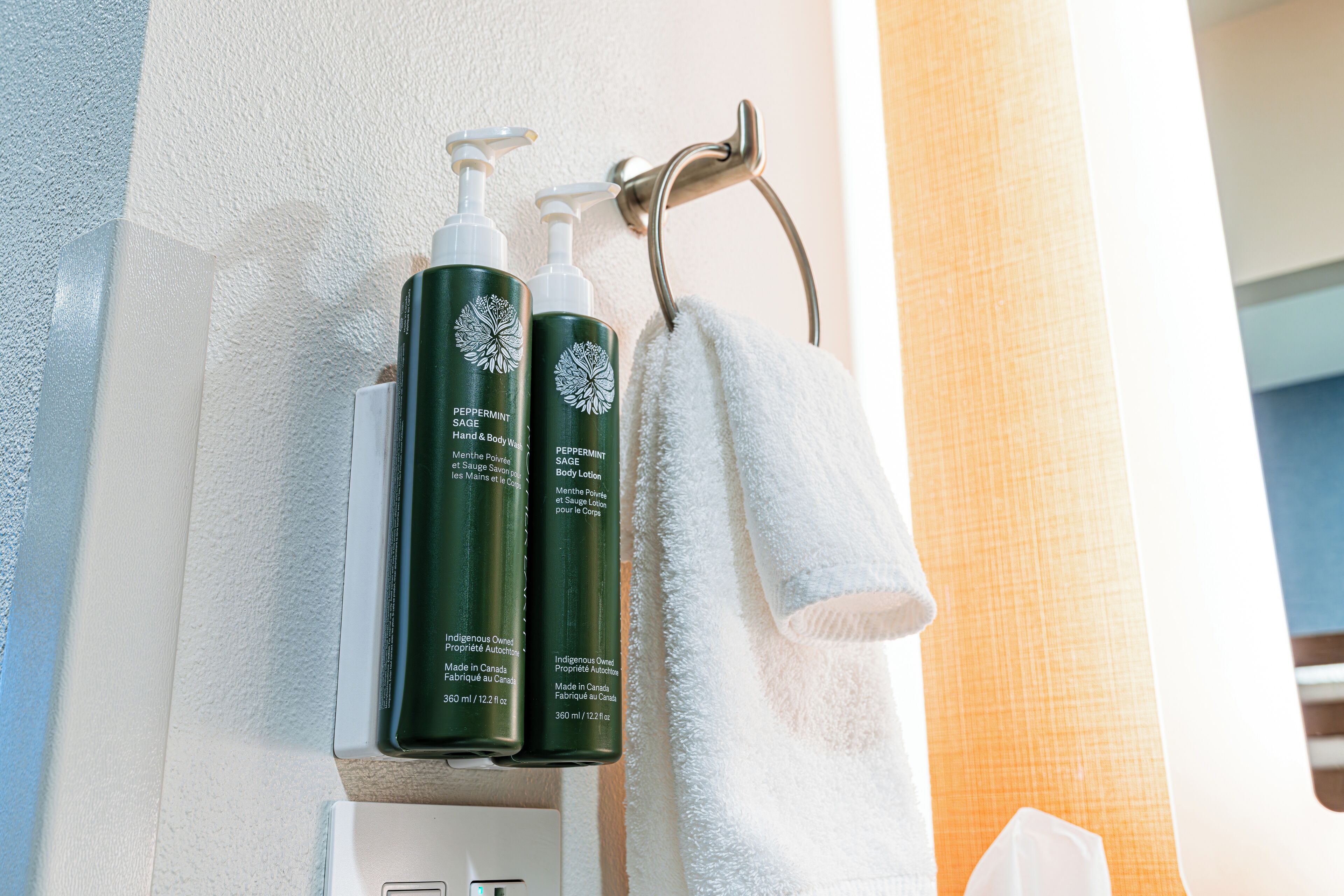 A bathroom with a towel rack holding a white towel and two bottles of body lotion.