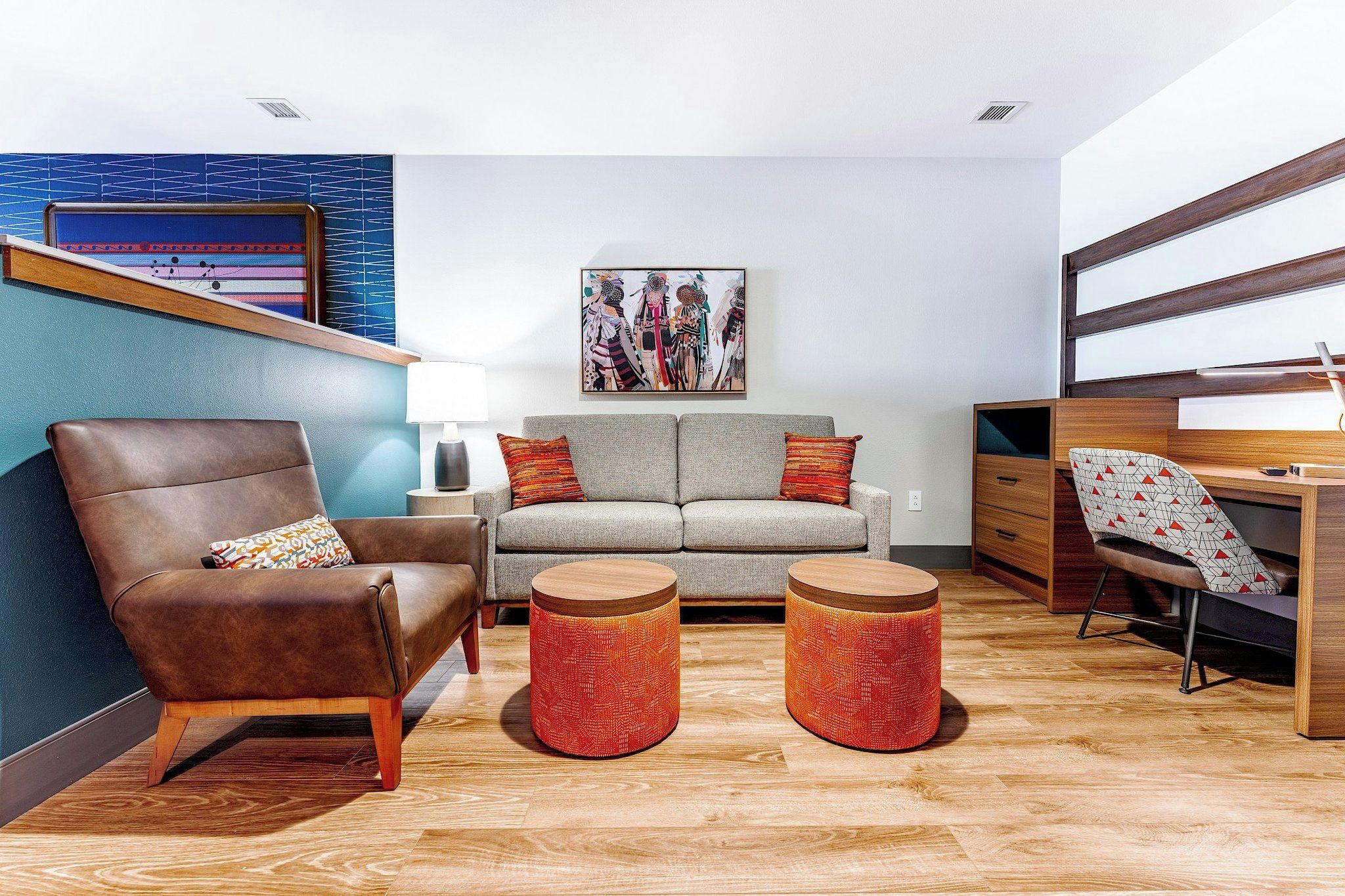 A modern living room with a brown leather armchair, a grey sofa, two wooden side tables, and a wooden desk with a chair.