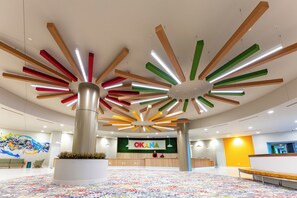 A spacious lobby with a colorful abstract mural, a reception desk, and a unique ceiling design with wooden beams and linear lights. - OKANA Resort & Indoor Waterpark (Oklahoma City)