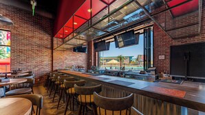 A bar area with a brick wall, wooden tables, and bar stools. - OKANA Resort & Indoor Waterpark (Oklahoma City)