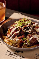 Egy tál nachos, melyet sajttal, szalonnával és zöldhagymával tettek ki, a háttérben pedig egy ital látható.