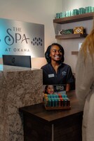 A reception desk with a sign for 'The Spa at Okana' and a display of 'COOLA Organic SPF Lipux.'