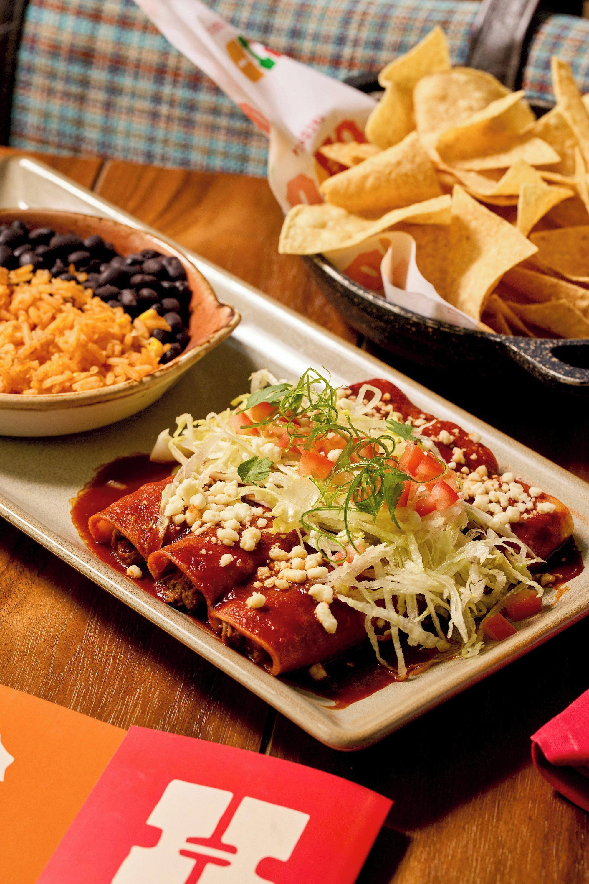 Une assiette d’enchiladas garnies, un bol de riz et de haricots, et un panier de chips de tortillas.