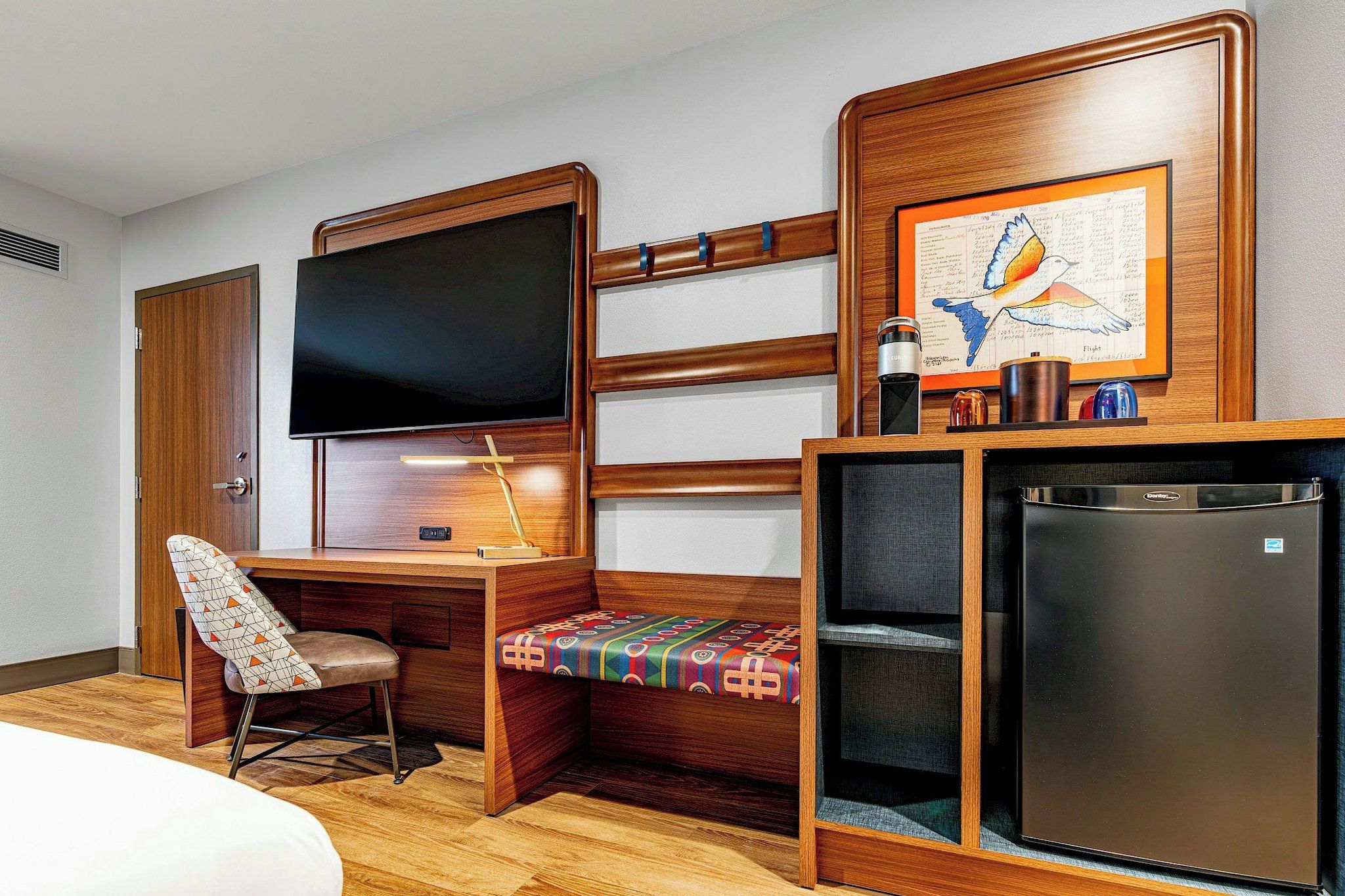 A hotel room with a wooden desk, a television, a small refrigerator, and a bed.