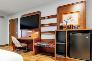A hotel room with a wooden desk, a television, a small refrigerator, and a bed. - OKANA Resort & Indoor Waterpark (Oklahoma City)