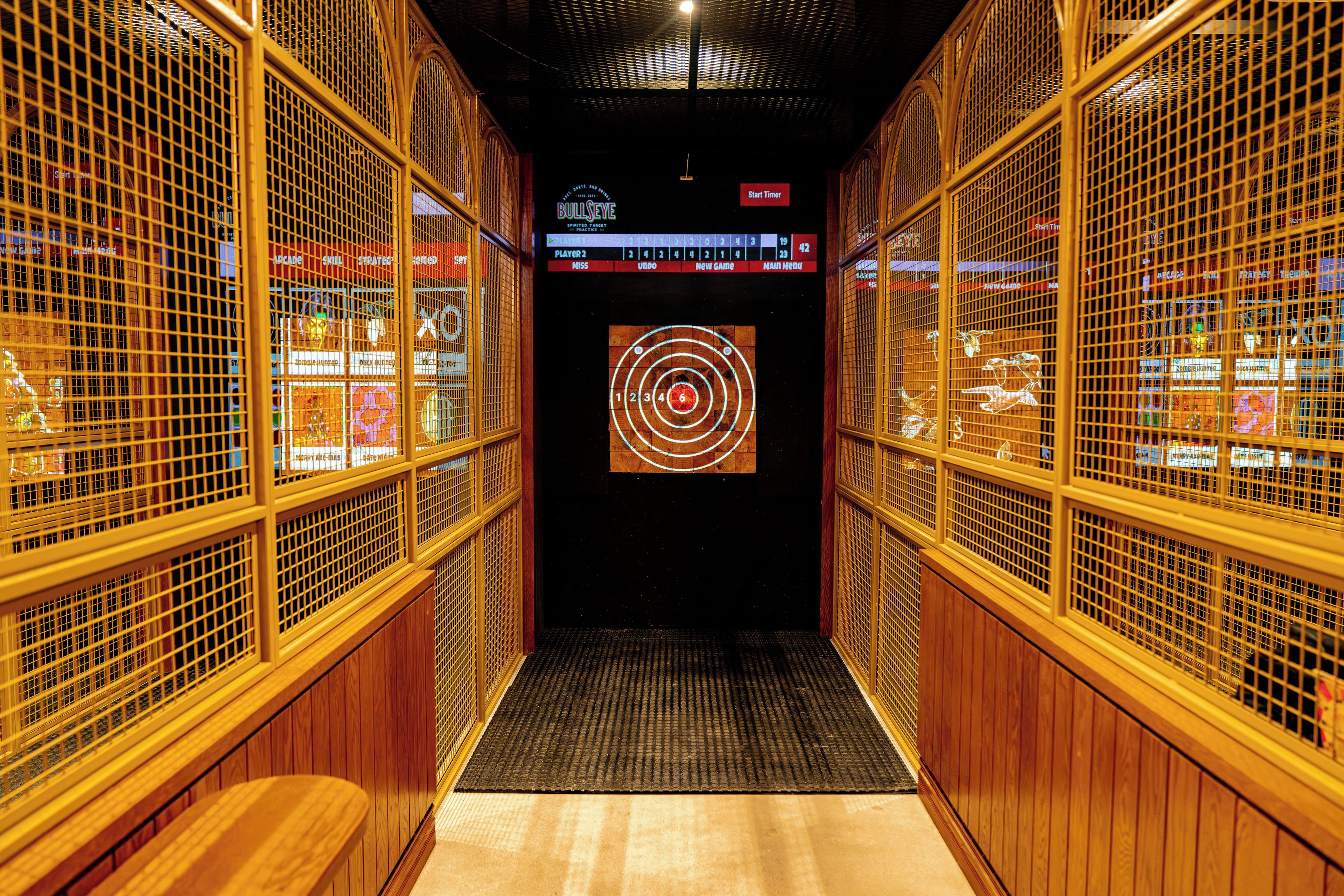 A corridor with wooden paneling and metal grilles, leading to a room with a dartboard.