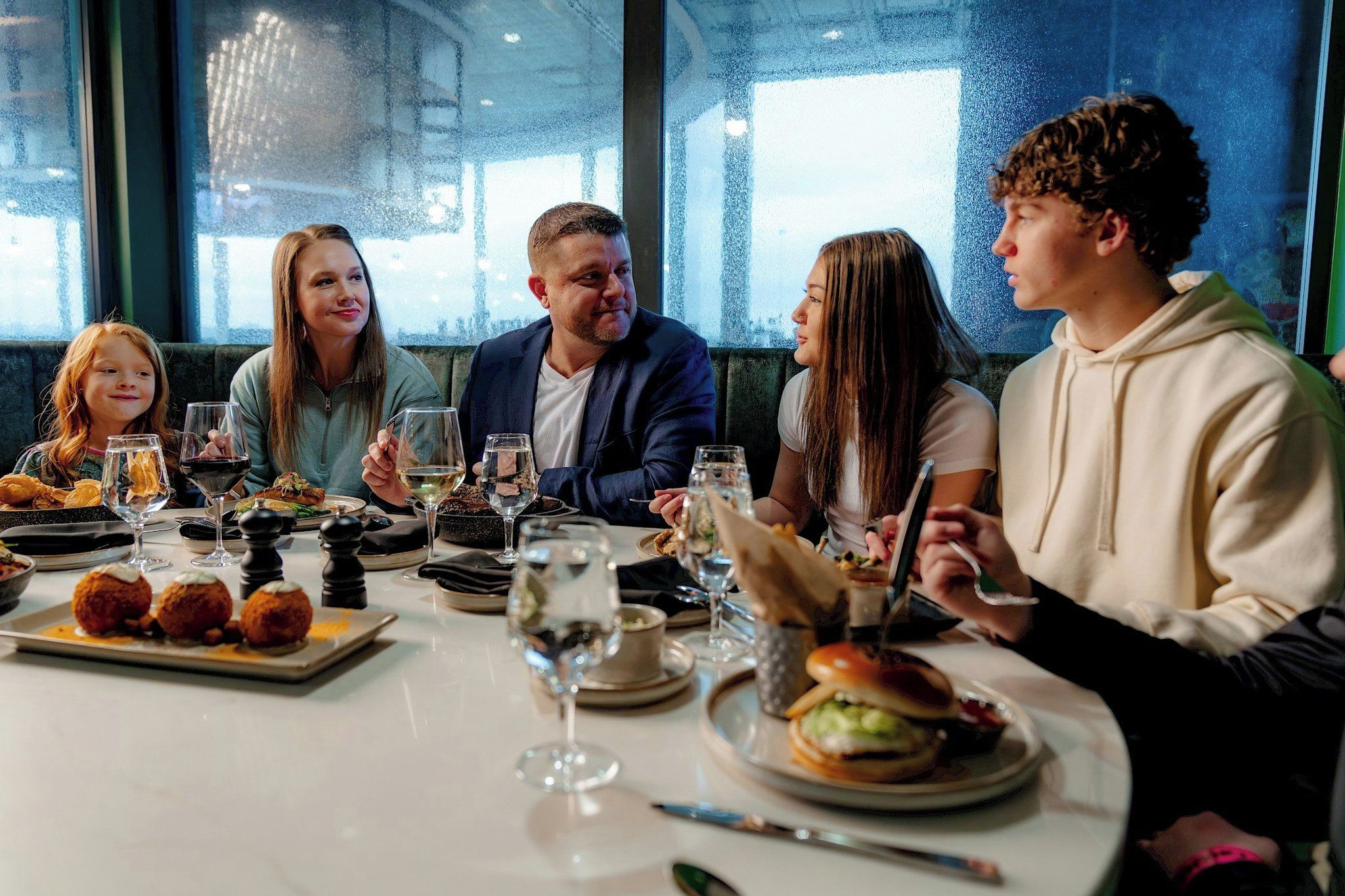 Un groupe de personnes est réuni autour d’une table, où se trouvent divers plats et boissons.