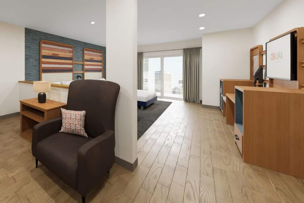 Ein modernes Hotelzimmer mit Sofa, Sessel, Holzbeistelltisch und Schreibtisch mit Computer.