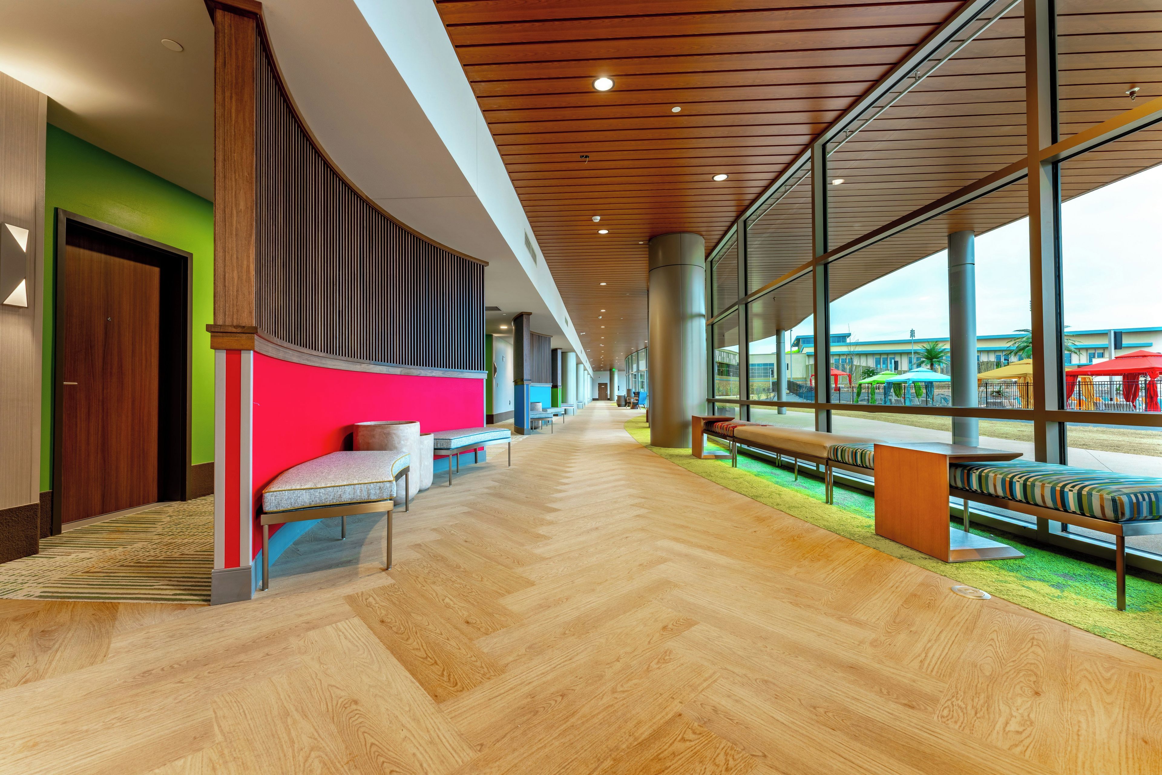 A spacious corridor with wooden flooring, seating areas, and large windows offering views of the outside.
