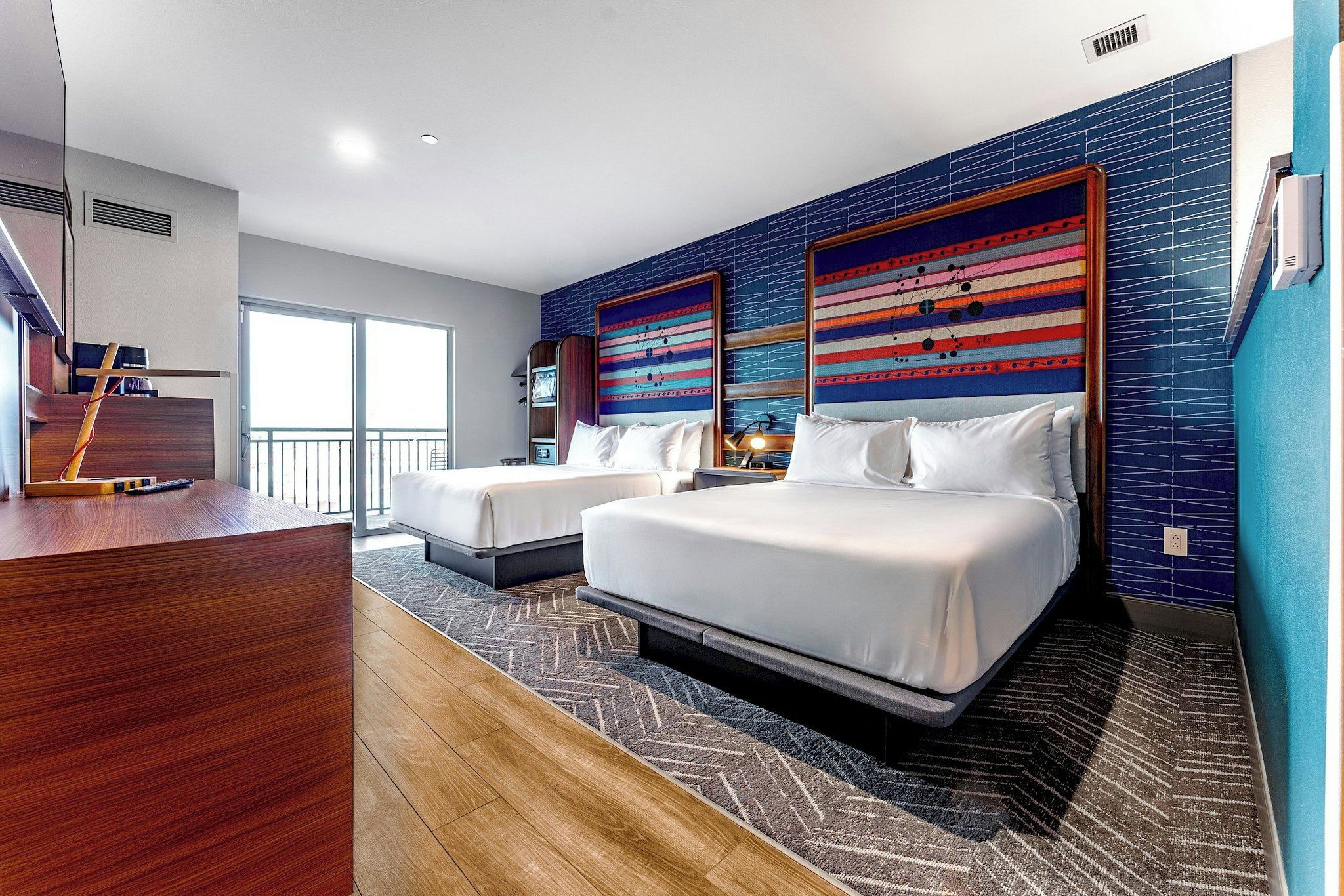 A hotel room with a large bed, a smaller bed, a desk, and a balcony.