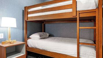 Un lit superposé avec une structure en bois, une table de chevet avec une lampe et un mur gris.