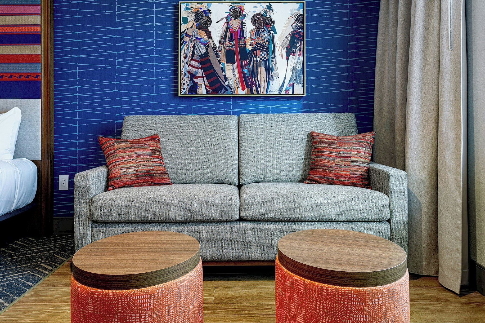 Ein modernes Wohnzimmer mit einem grauen Sofa, zwei runden Holztischen und einem farbenfrohen abstrakten Gemälde an der Wand.