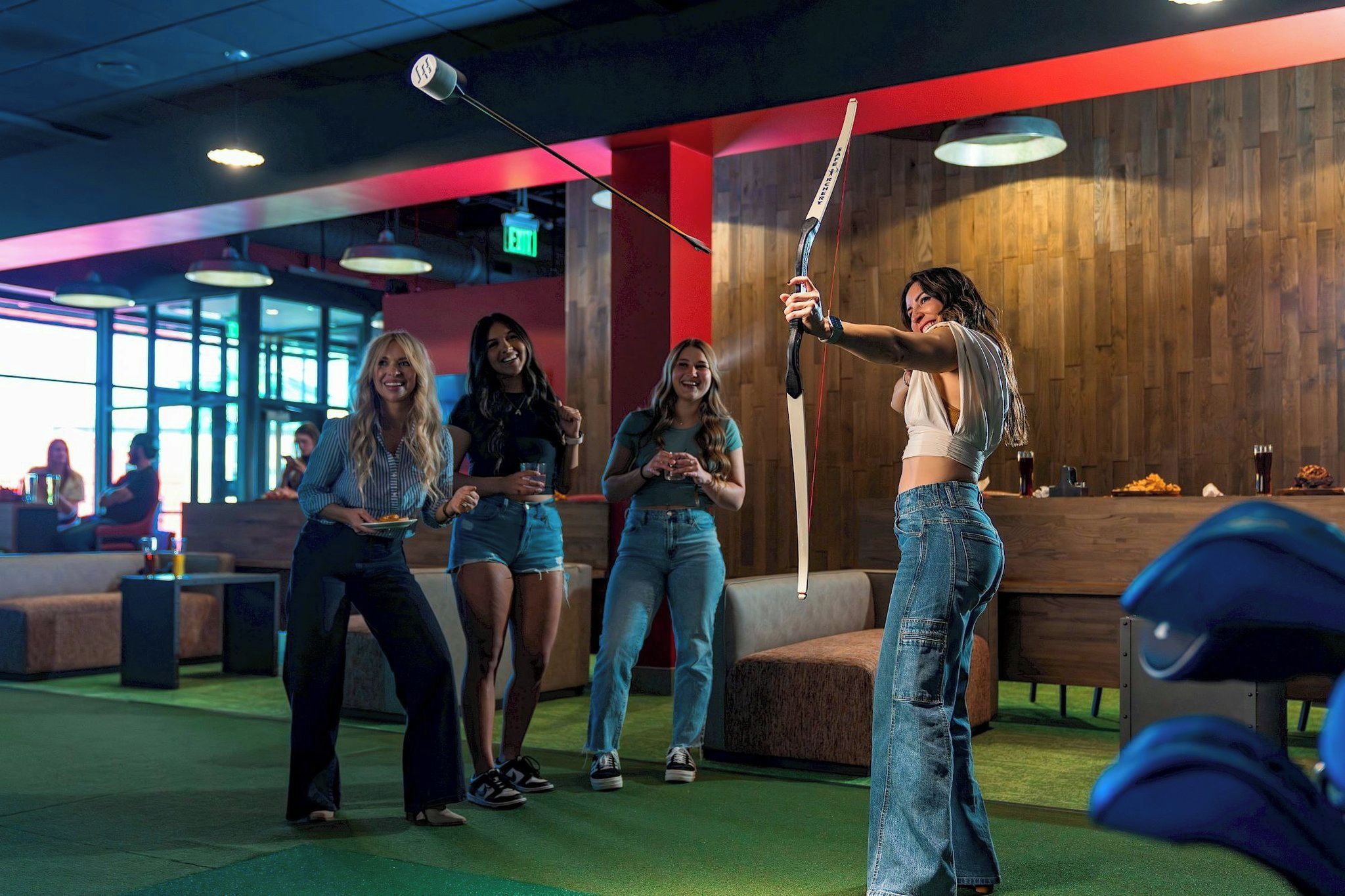A group of people in a casual indoor setting with a wooden wall and a green carpet.