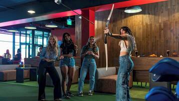 A group of people in a casual indoor setting with a wooden wall and a green carpet.