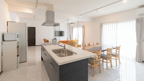 Cozinha moderna com ilha central, eletrodomésticos embutidos e área de jantar com mesa e cadeiras.