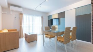 Uma sala de estar moderna com mesa de jantar de vidro, mobiliário de vime, televisão de tela plana e uma grande janela com cortinas.