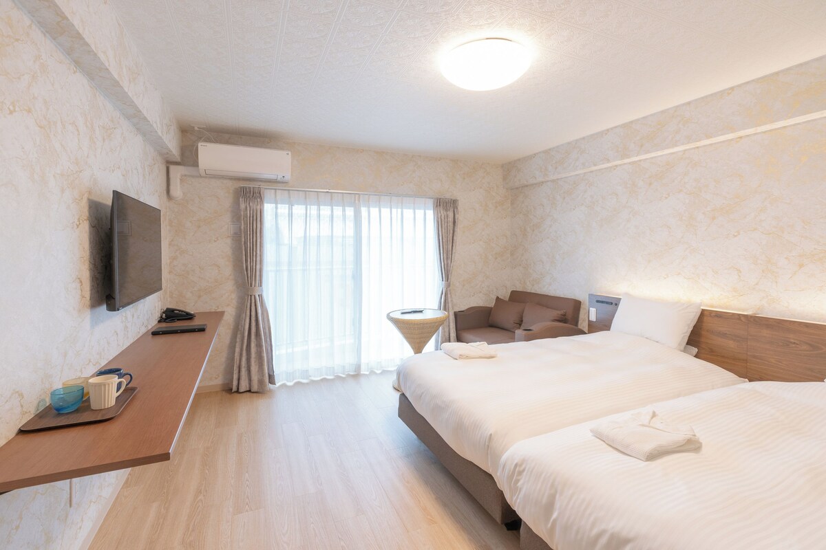 Een hotelkamer met een groot bed, een bureau met een flatscreen televisie, een zithoek met een stoel en een klein tafeltje, en een raam met gordijnen.