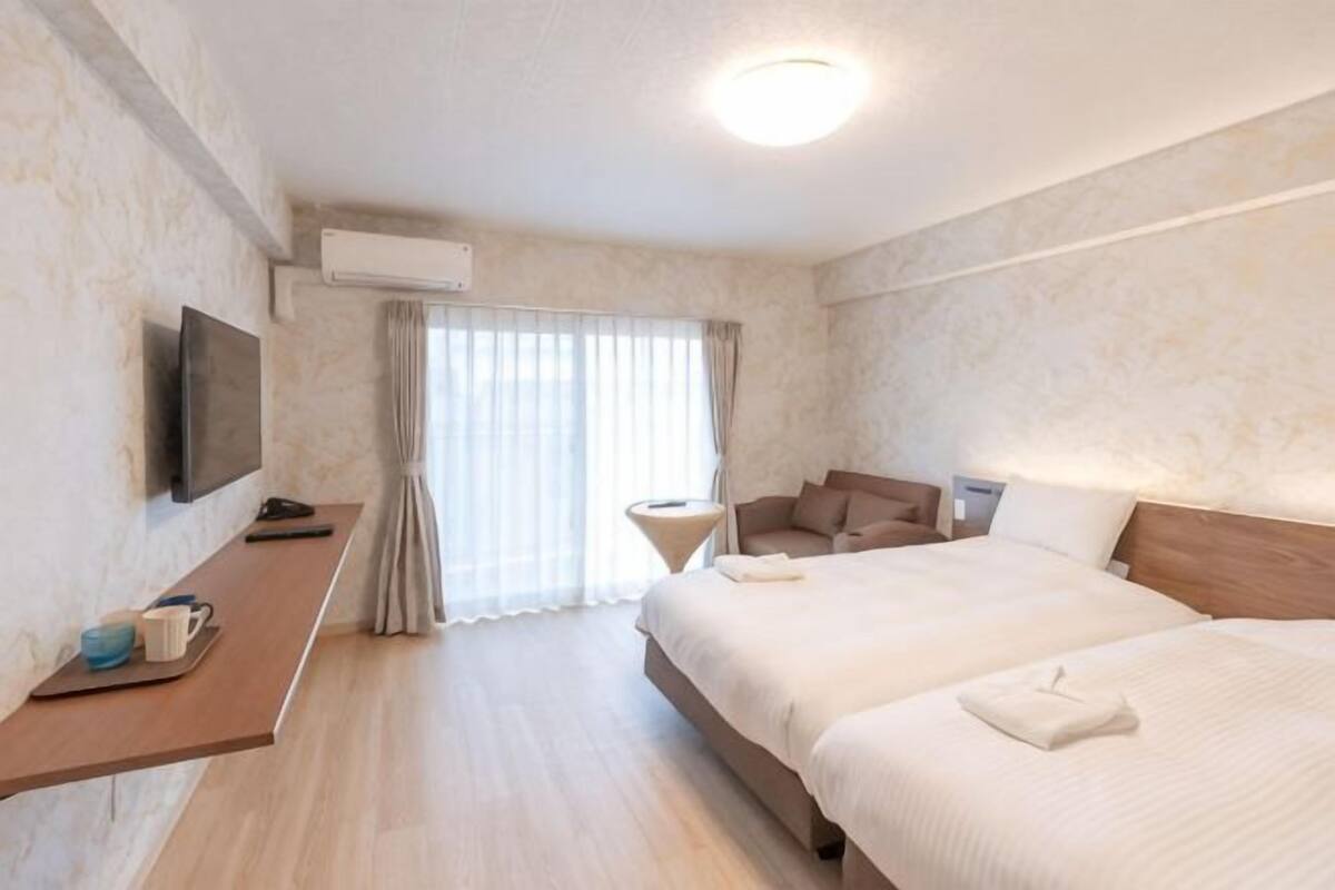 Ein Hotelzimmer mit Bett, Schreibtisch, Flachbildfernseher, Stuhl und einem Fenster mit Vorhängen.