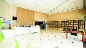 Um saguão de hotel com balcão de recepção, área de estar e uma estante cheia de livros e objetos decorativos.