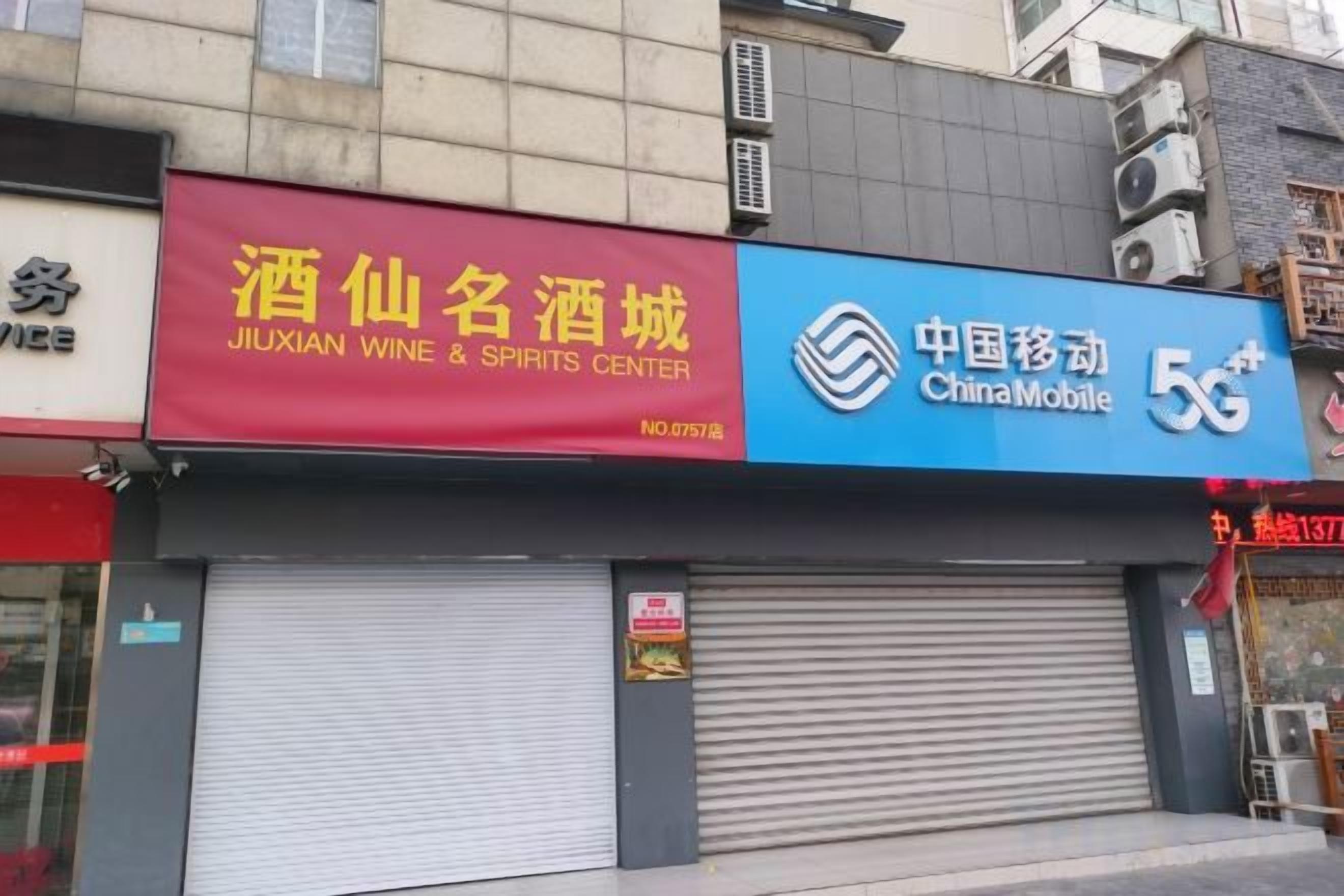 A storefront with a red sign for Jiuxian Wine & Spirits Center and a blue sign for China Mobile 5G.