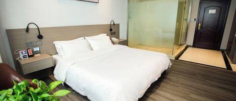 Una habitación de hotel con una cama, mesita de noche, lámpara y una planta en maceta.