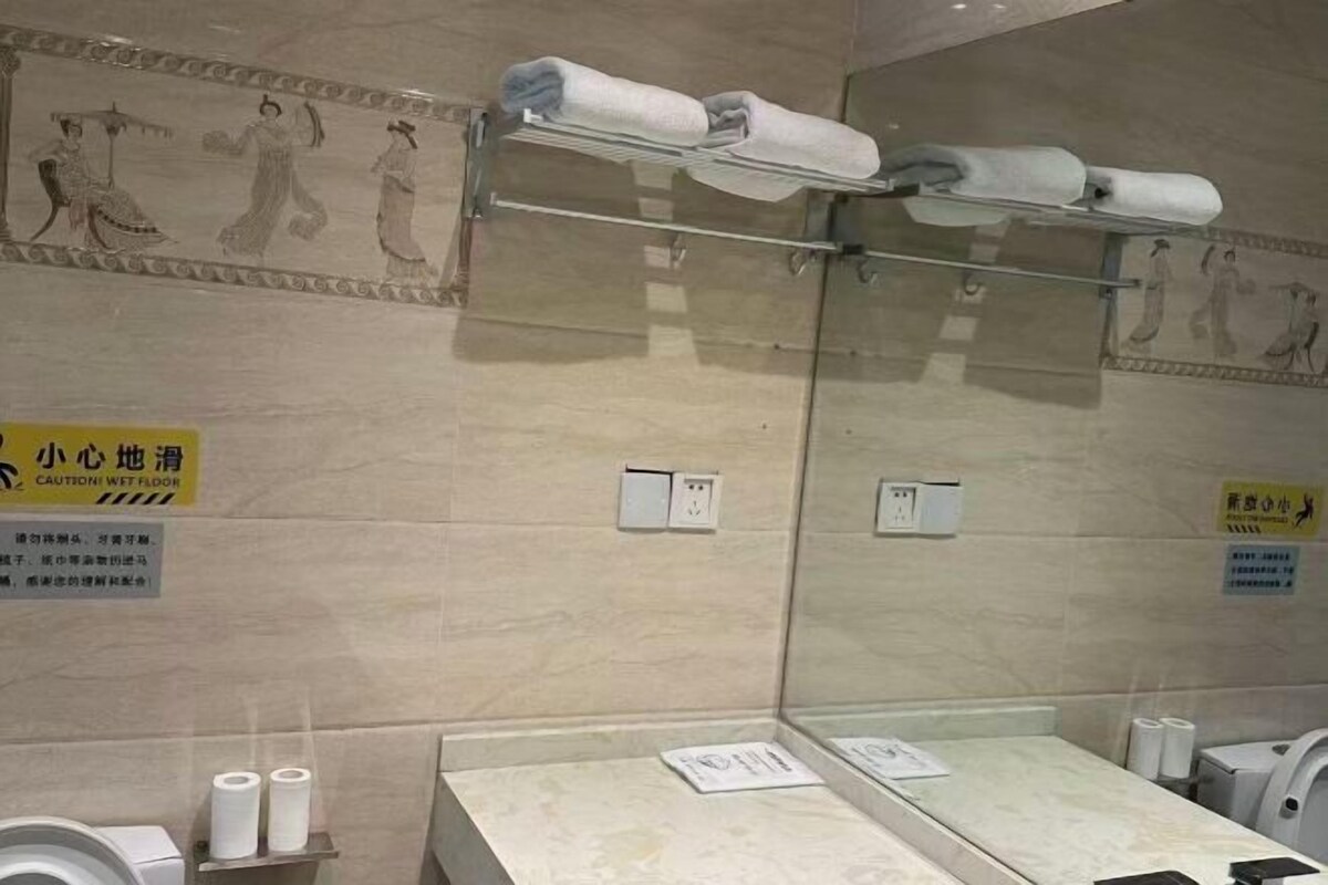 A bathroom with a wet floor sign, towel racks, toilet paper, and a mirror.
