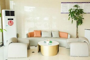 Een moderne woonkamer met een bank, poefjes, een salontafel en een potplant.