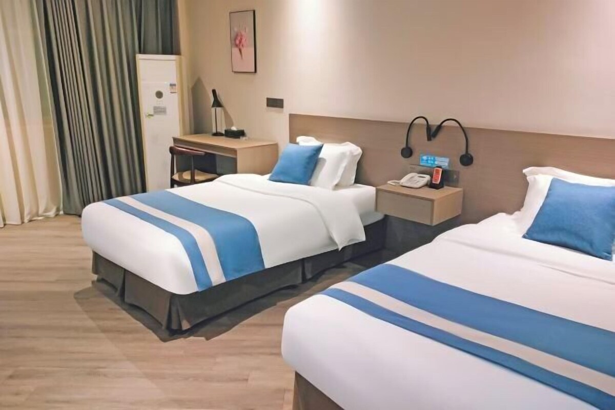 A hotel room with two beds, a desk, a chair, a telephone, and a wall-mounted lamp.