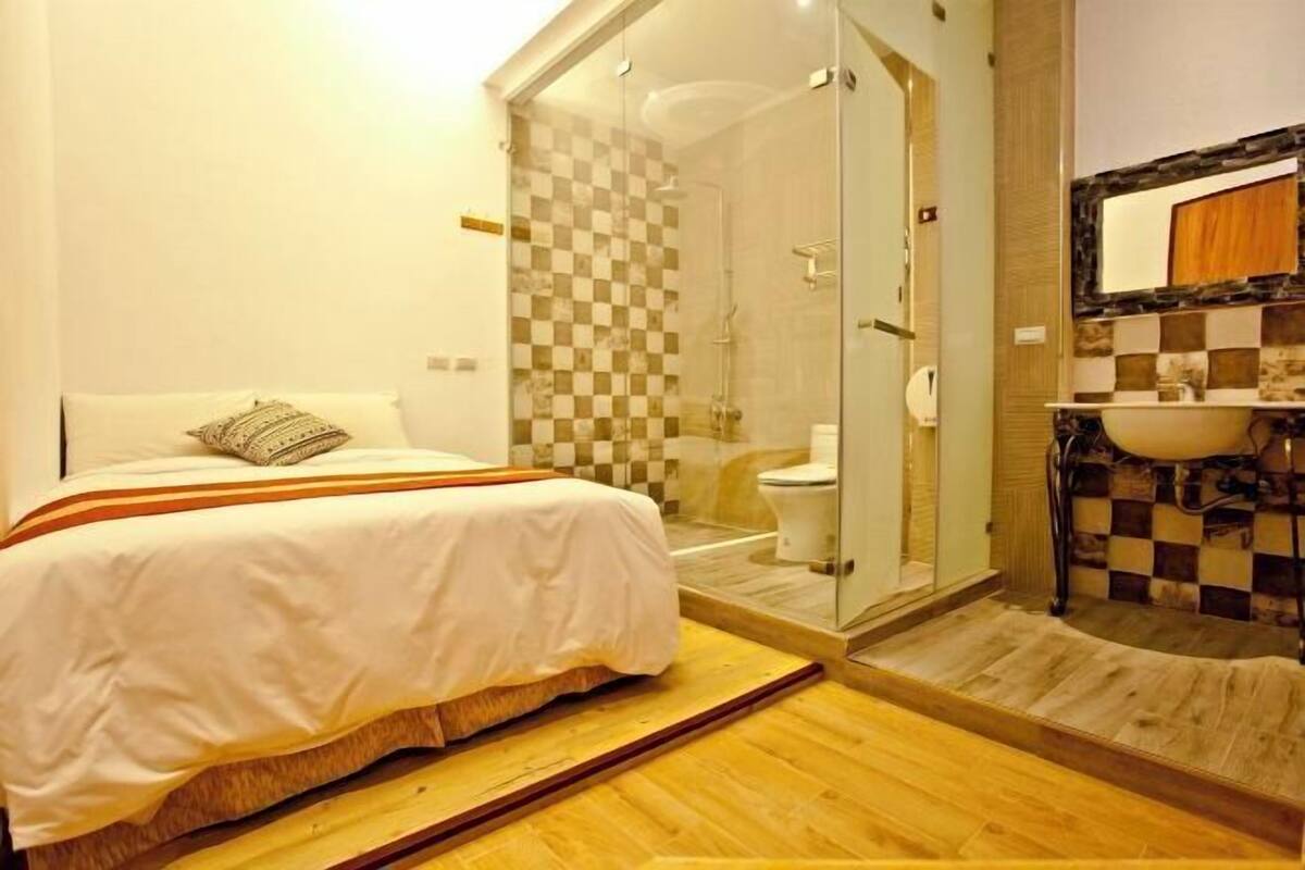 A hotel room with a bed, a shower, and a bathroom with a sink and mirror.